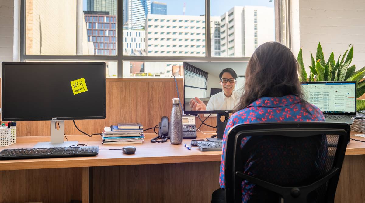 Employees in an office with some working from home, visible on screen, and some in the office physically